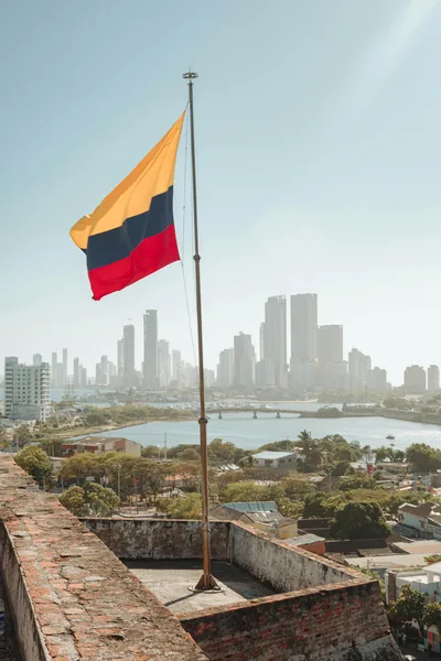 Colombian flag waving against the modern skyline of Cartagena, Colombia, under a bright blue sky.