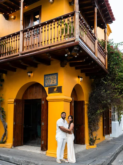 Happy couple embracing outside a vibrant yellow building with wooden balcony in a lively street.