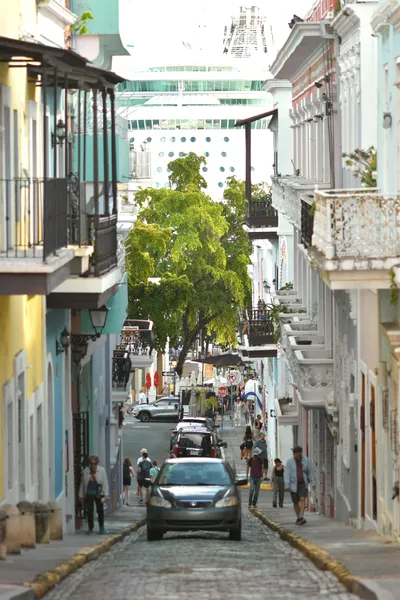 A lively street scene in San Juan with vibrant buildings and a towering cruise ship in the background.