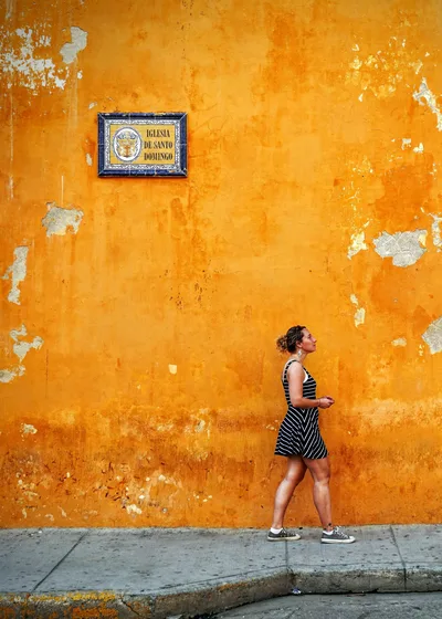 Stylish woman strolls by a vibrant, textured wall in Cartagena, Colombia.