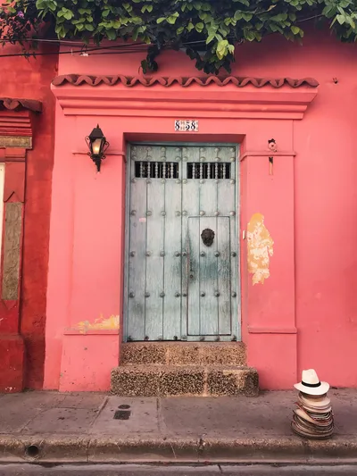 A vintage wooden door set against vibrant pink walls in Cartagena. Perfect for travel inspiration.